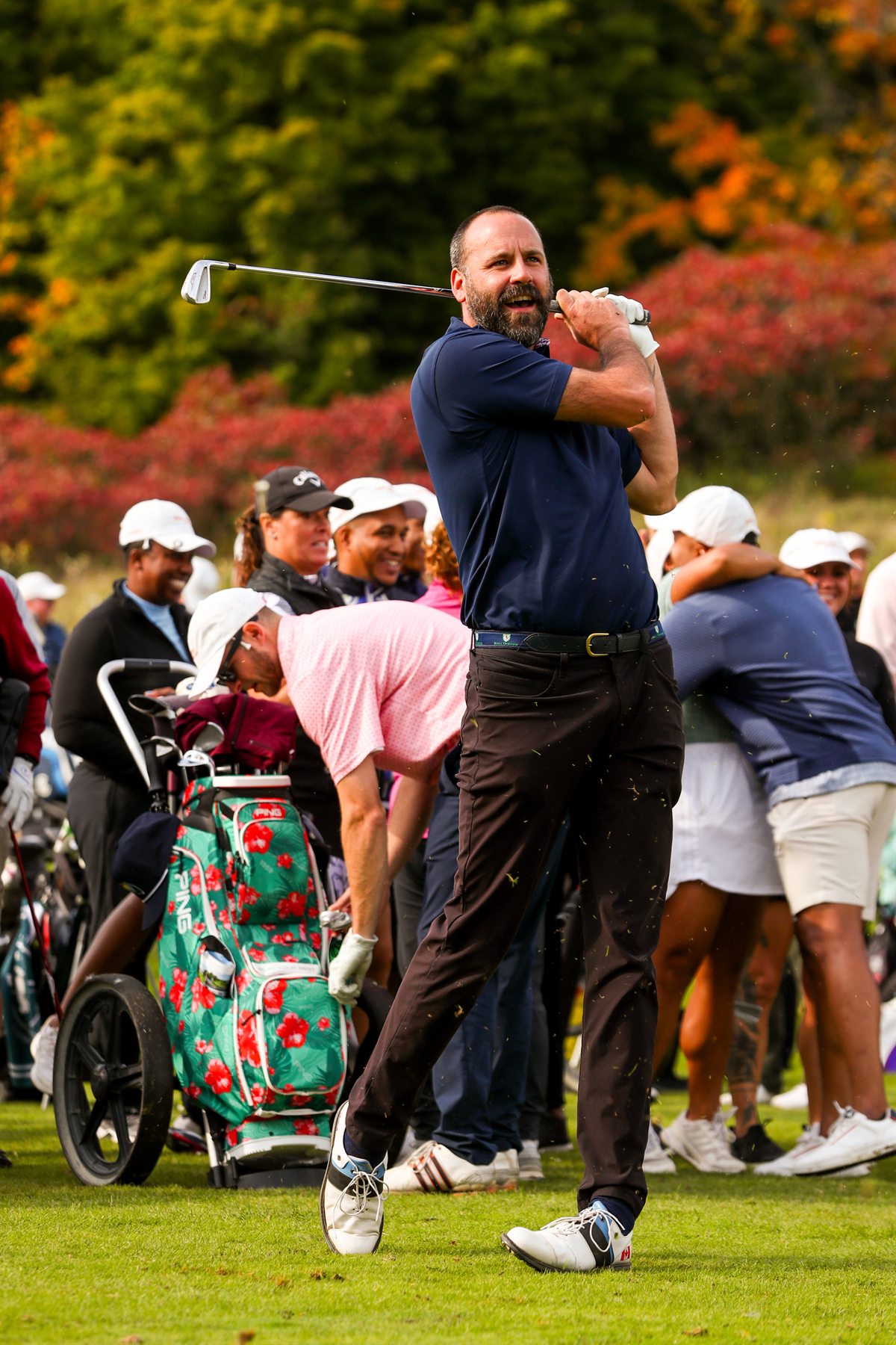 Joe on a golf course completing a swing in front of a tournament crowd.